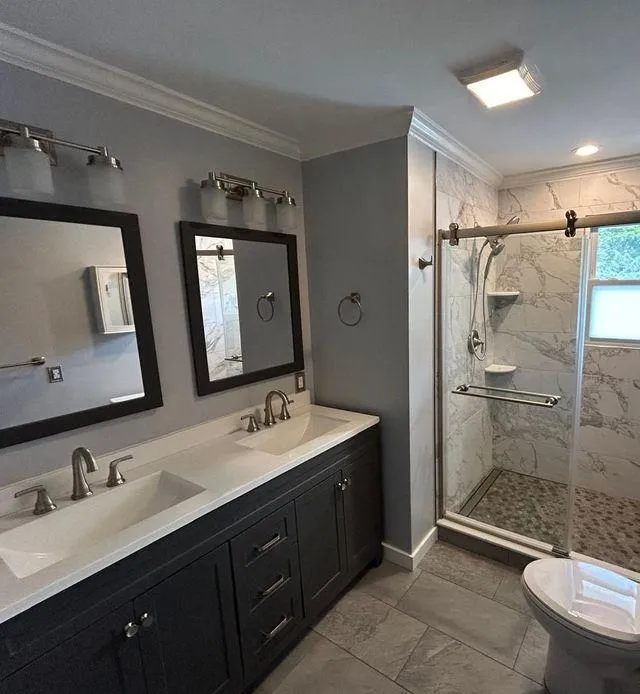 Bathroom featuring marble walls, a spacious shower, and a double sink vanity.