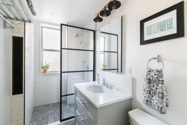 Black and white tiled shower in a renovated bathroom, white vanity with silver fixtures.