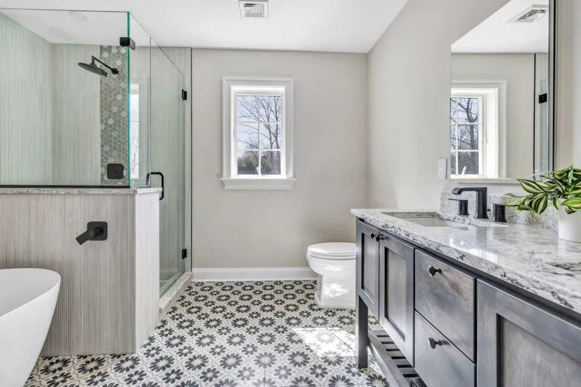 Bathroom with a contemporary design, including a large mirror above the sink, a walk-in shower with clear glass doors, and a marble floor.