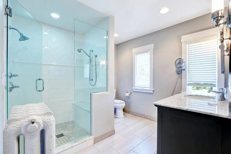 Bathroom renovation showcasing a contemporary design with clear glass shower, pristine white vanity, and stylish fixtures.