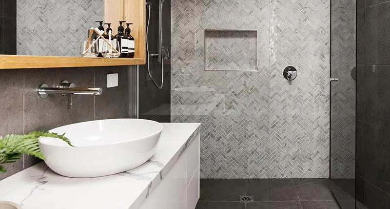 Bathroom renovation with contemporary finishes, including a glass shower enclosure, white vanity, and dark flooring.