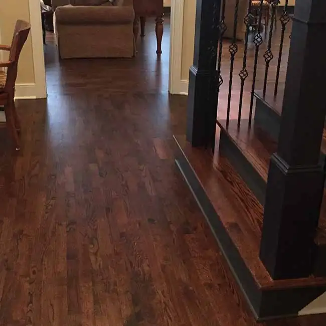 Hardwood flooring with a dark brown color and a smooth finish, installed on the ground level and transitioning to a staircase.