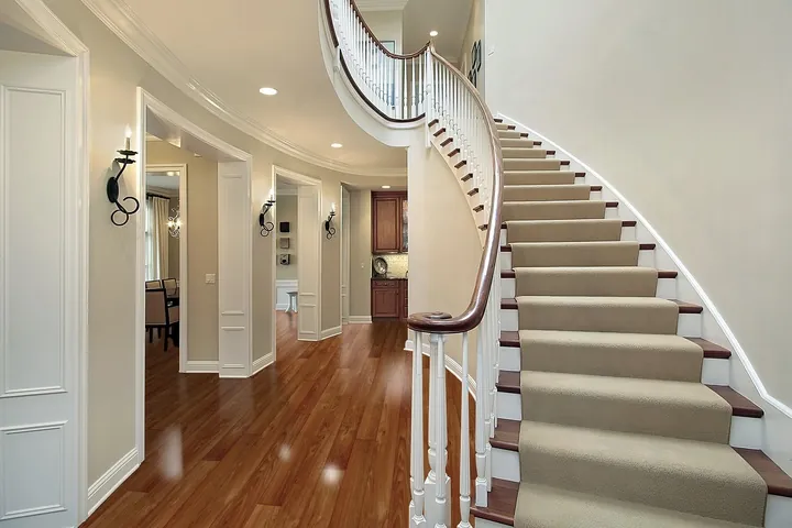 The hardwood flooring is a rich brown color with a smooth finish, featuring a herringbone pattern that transitions seamlessly into the staircase and runner.
